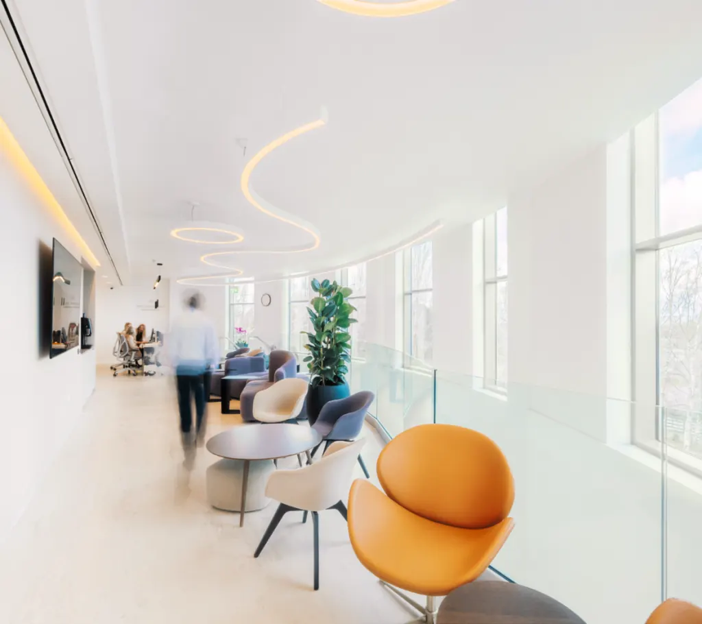 Sunlit upper-floor lounge at the Waterfront Private Hospital — orange and cream tulip chairs, floor-to-ceiling windows, sculptural ceiling lights.